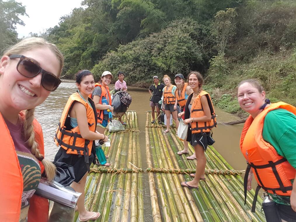 A group of volunteers stand on a bamboo raft in a river.