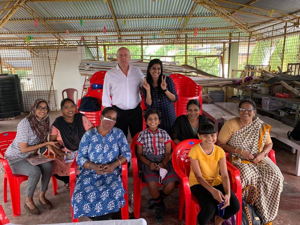 A man stands with a group of women seated in chairs.