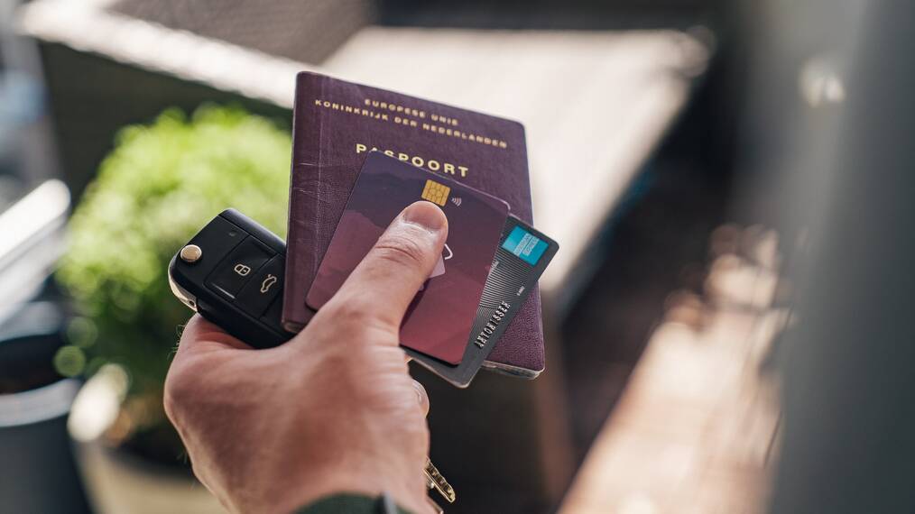 A hand holding two credit cards, a passport, and keys