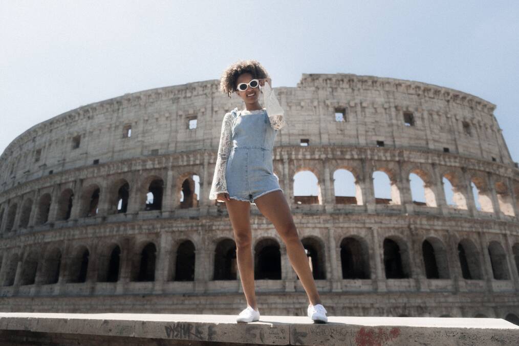 A woman stands smiling and posing in front of the Colosseum in Rome, Italy.