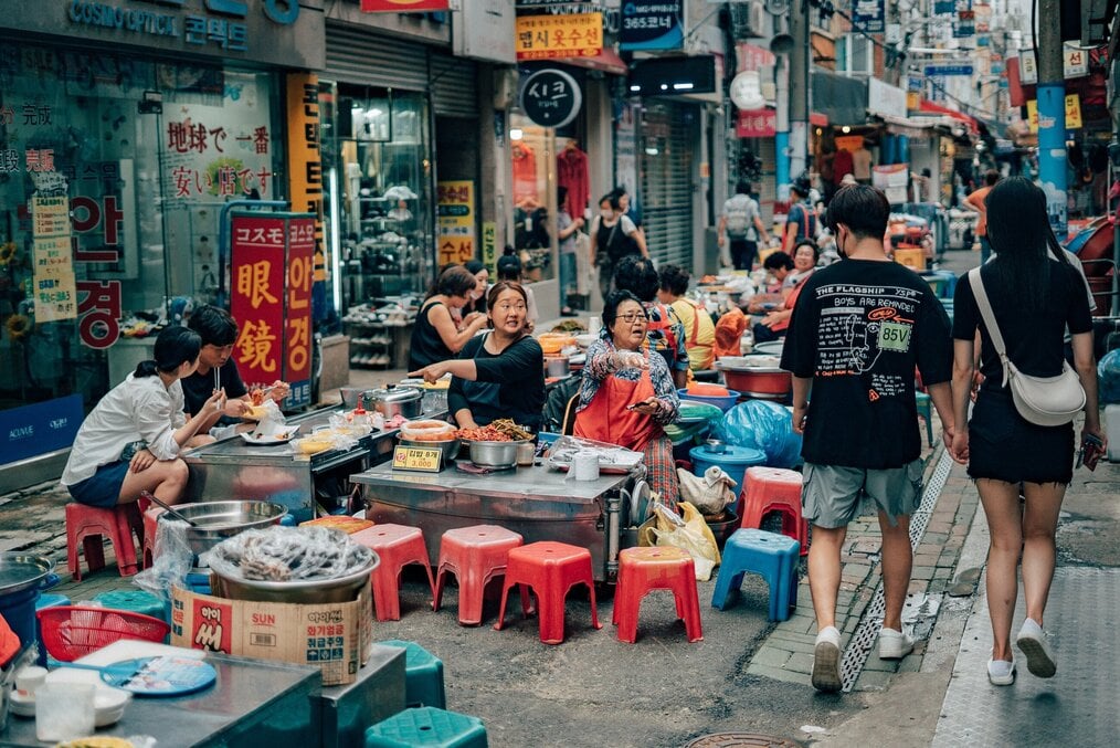 A couple holding hands walks through a crowded market in South Korea.