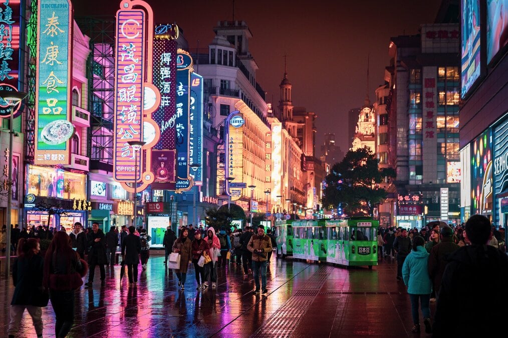 People walk down a crowded street with neon signs at night in China.