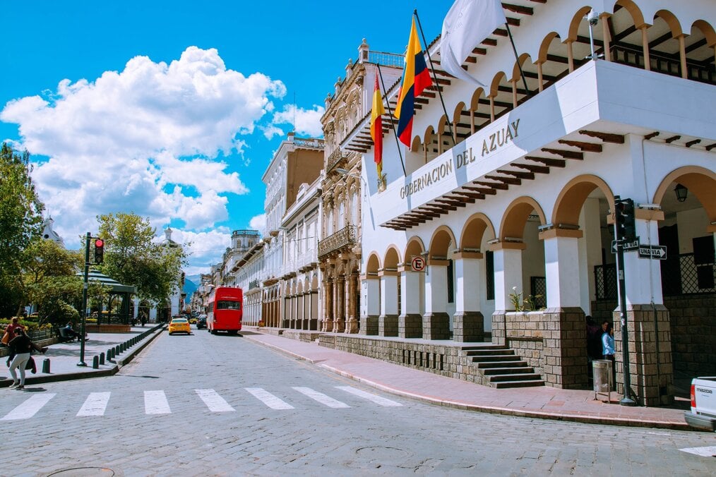 White buildings line a street under blue skies in Cuenca, Ecuador.