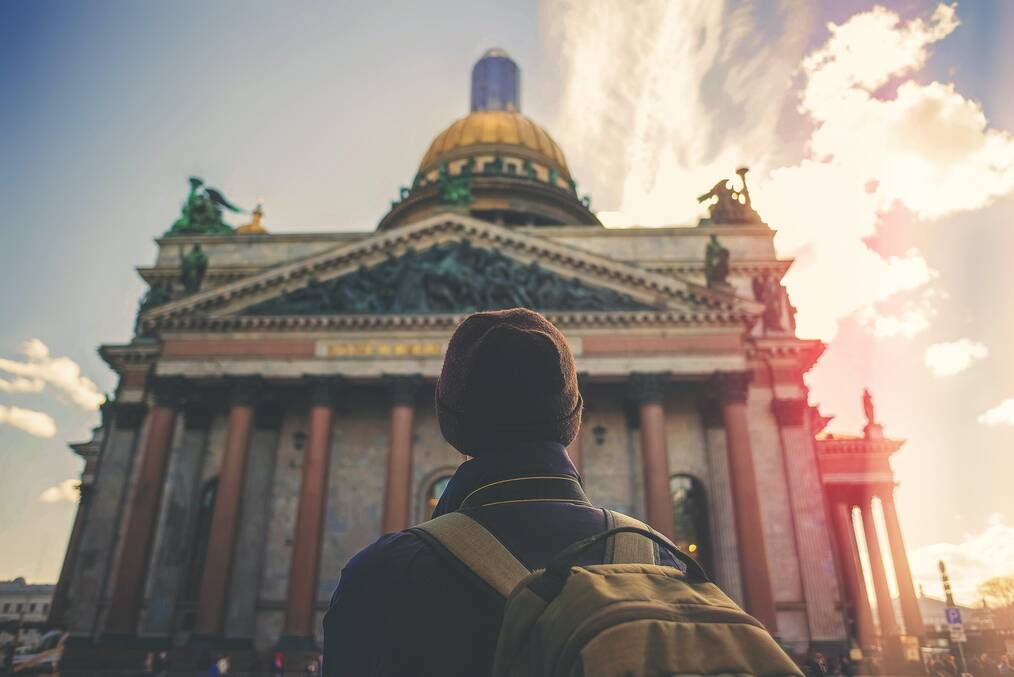A study abroad student wearing a red beanie and a green backpack facing a building in Germany