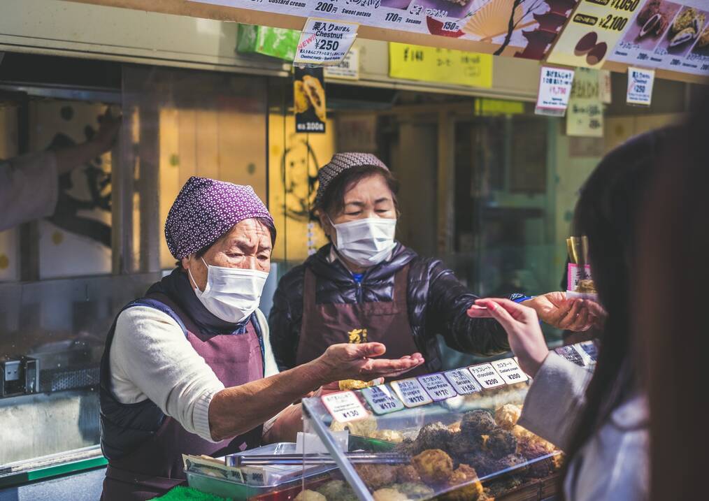 Two women with face masks serve a customer at a street food stall.