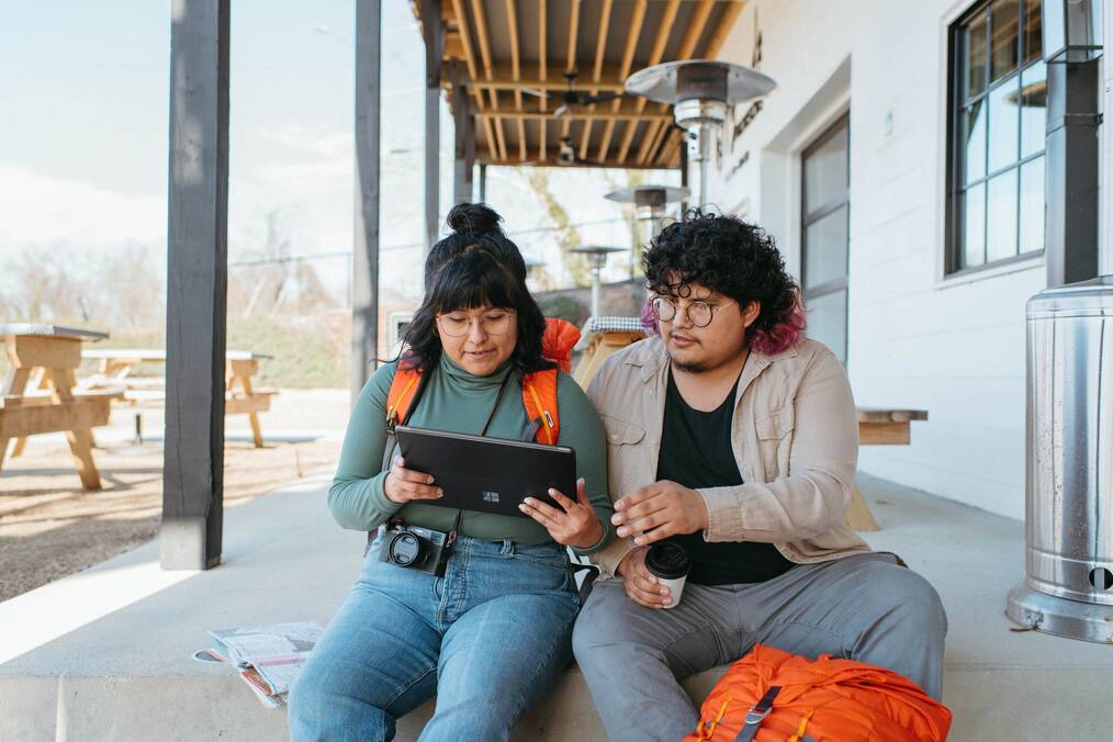 A man and a woman sit on a porch and look at a tablet together.