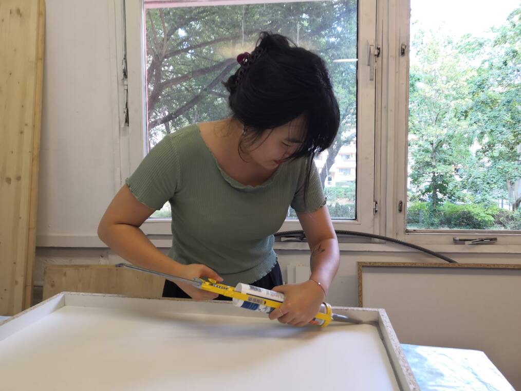 A woman uses a caulking gun on a frame.