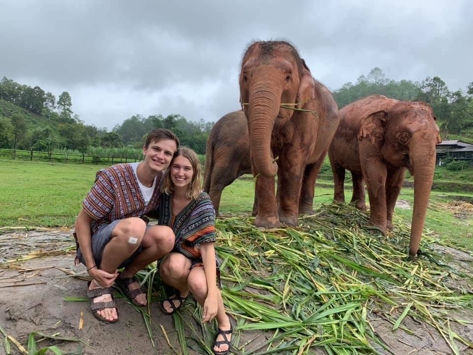 A man and a woman pose in front of three elephants.