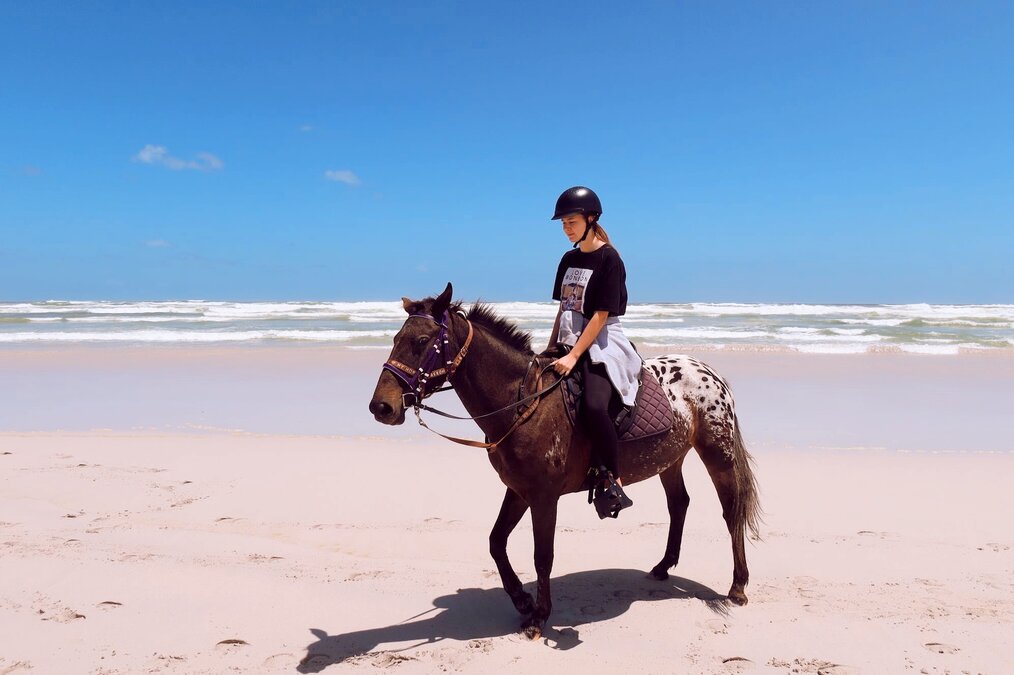 Rebecca, World Unite Internship in Ireland A woman rides a brown horse on a white sand beach.