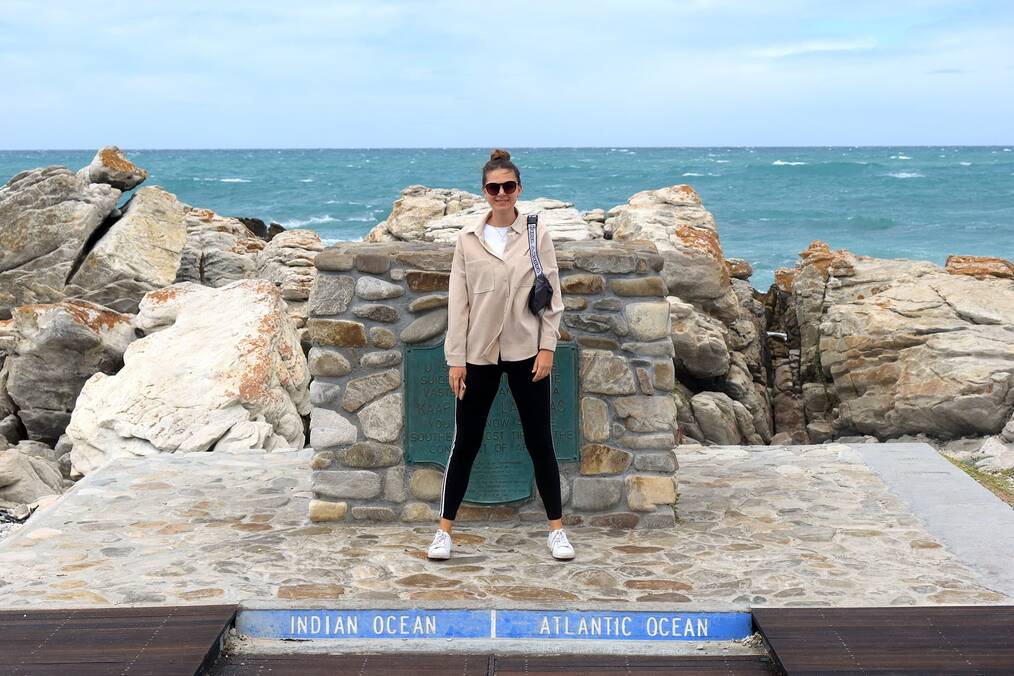 A woman stands with one foot over an Atlantic Ocean sign and the other foot over an Indian Ocean sign.