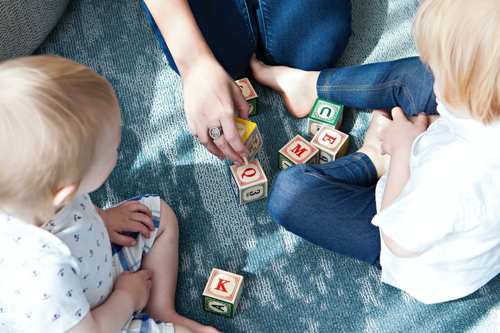 Photo by Marisa Howenstine on Unsplash A hand reaches for a block near two children on the floor.