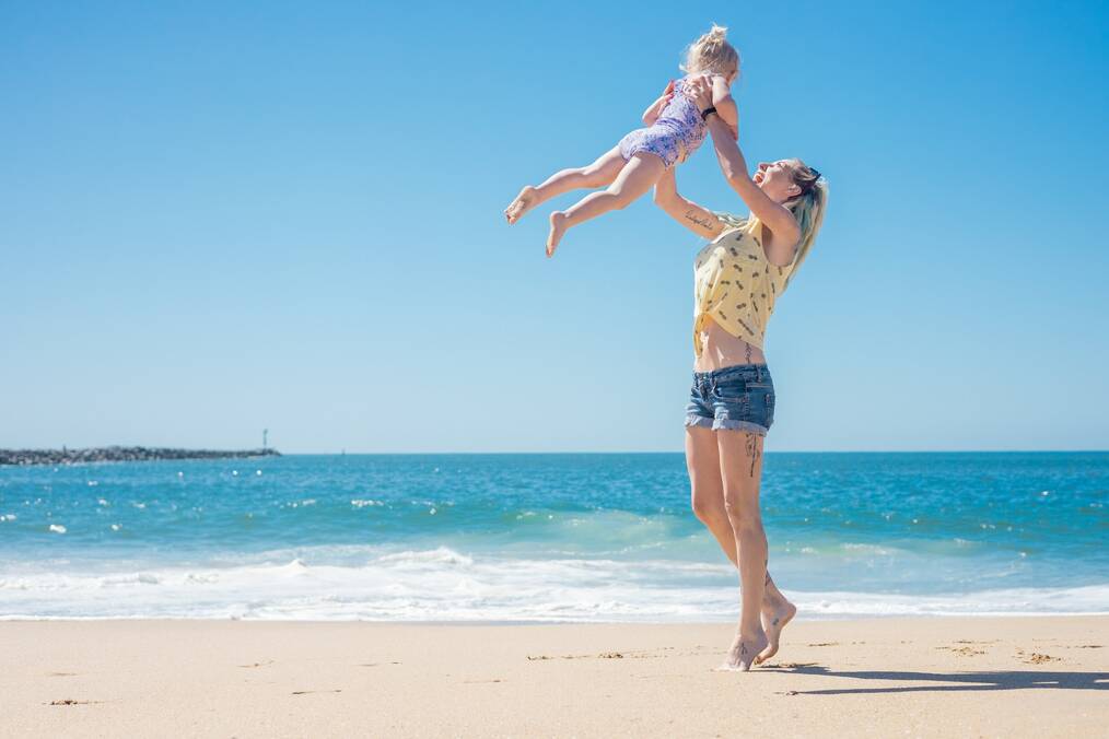A Woman Throwing Her Daughter in the Air while Standing on the Beach.