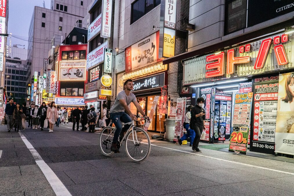 Photo by Sergio _snaps on Unsplash A man rides a bike on a street with bright neon signs in Japan.