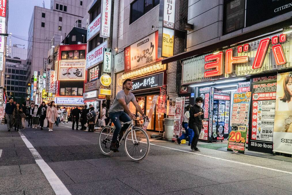 A man rides a bike on a street with bright neon signs in Japan.