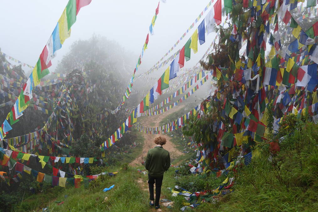 Theo Weiman walking on a mountain top in Nepal with colorful flags in the fog