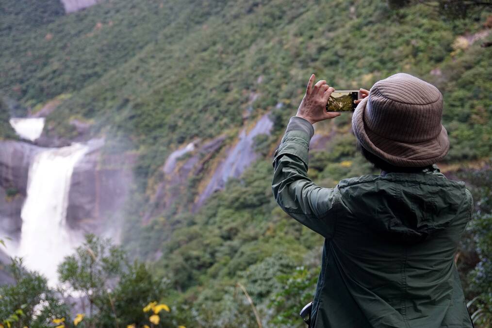 Person holding their phone and taking photo of waterfall