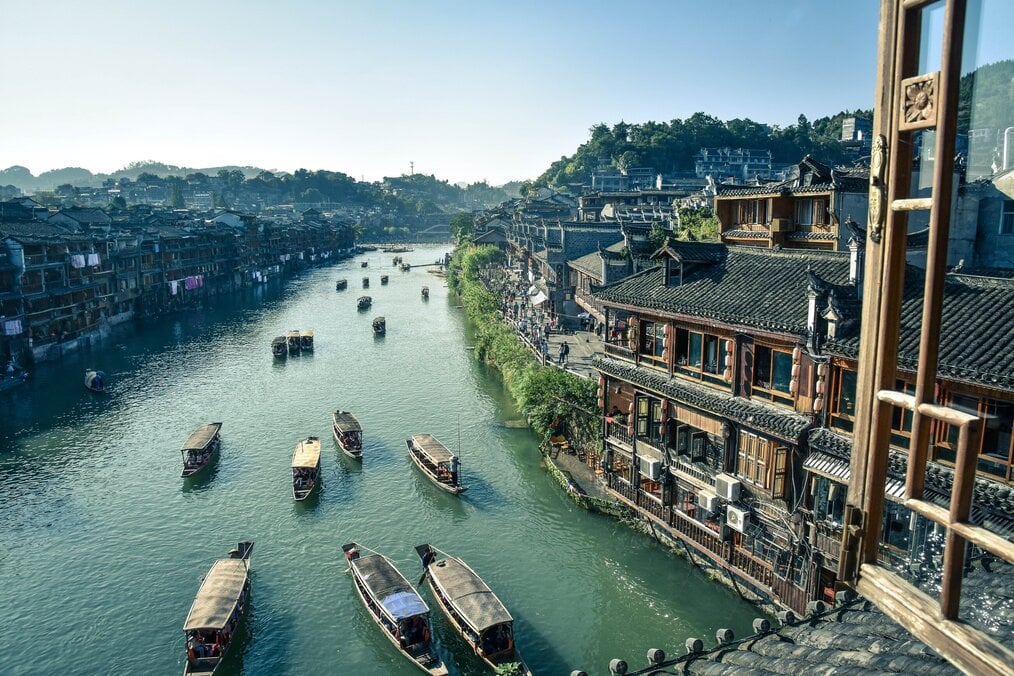 Photo by Emile Guillemot on Unsplash A drone shot of boats sailing down a river beside tall buildings.