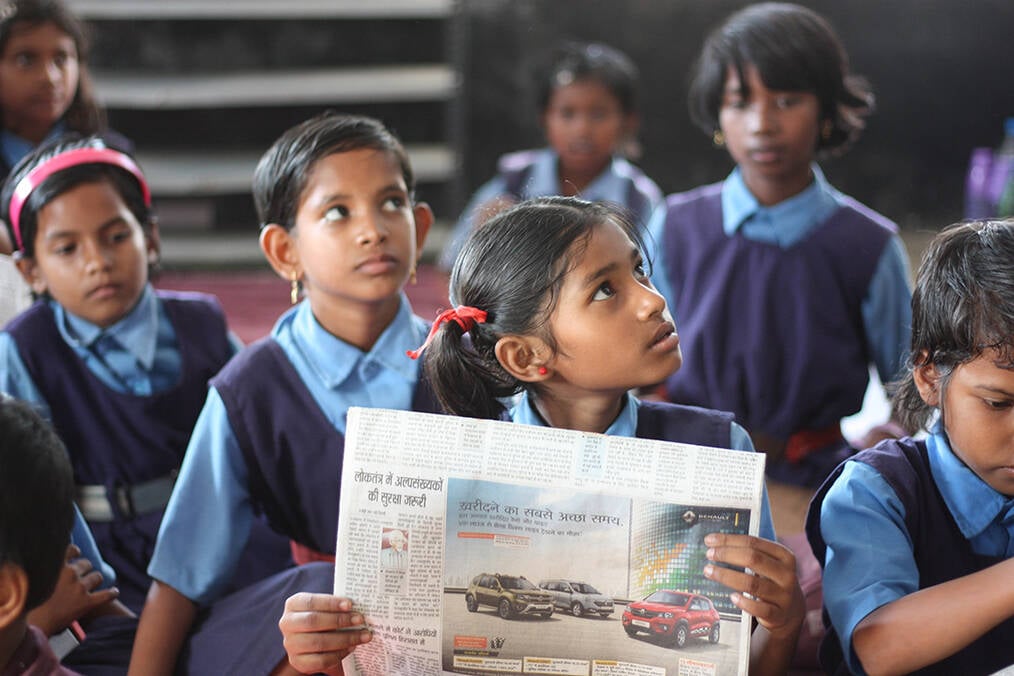 A class of young students looking at a newspaper