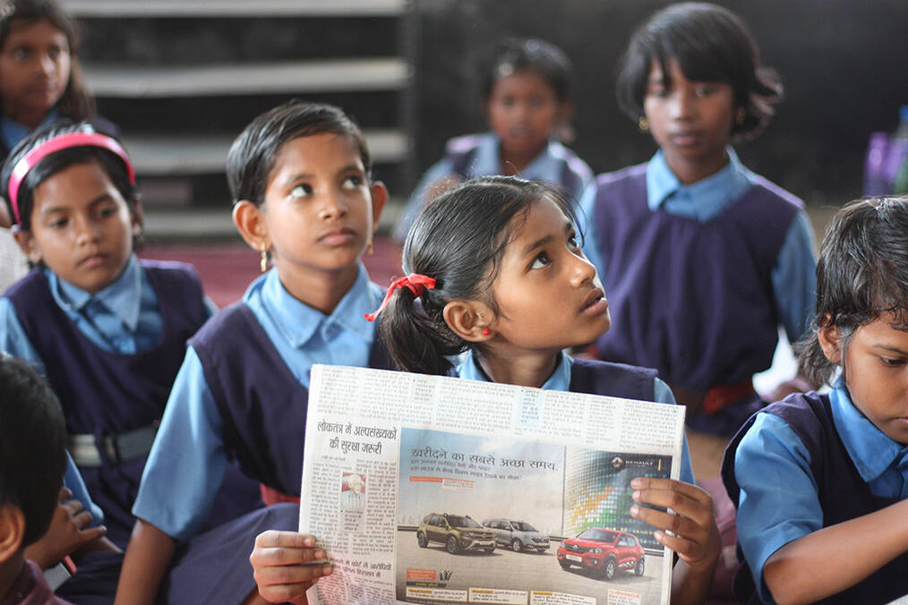 A class of young students looking at a newspaper