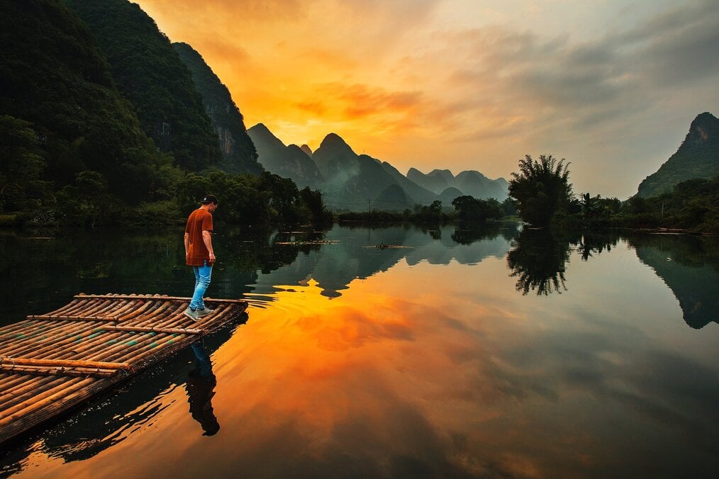 Photo by Joshua Earle on Unsplash A man stands on a raft on a river with a yellow sunset and mountains in the background.