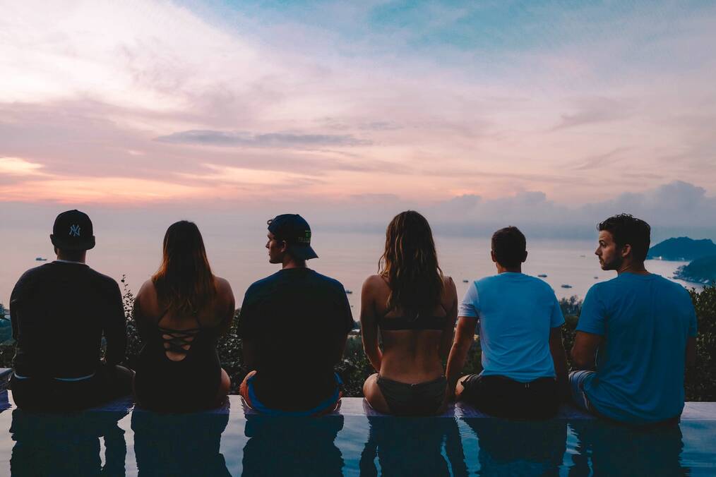 Study abroad students sitting at the edge of an infinity pool looking out at the pink an blue sunset together