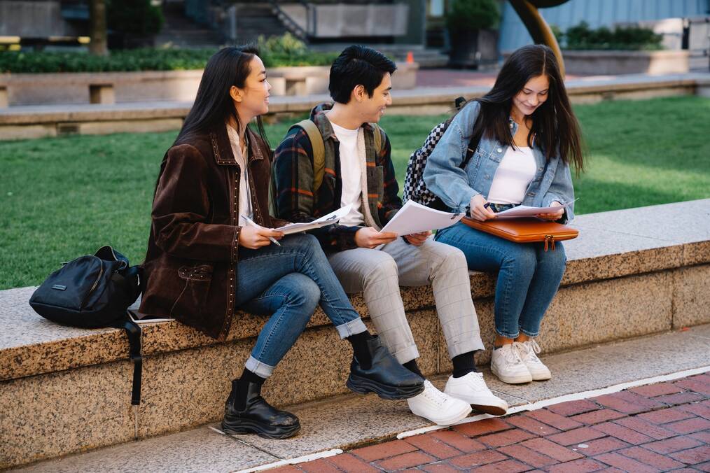 Three students sitting next to each other outside on campus