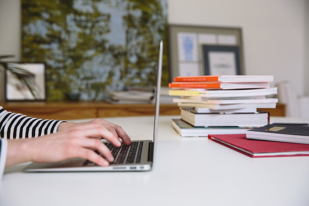 Person typing on laptop, stacked books on desk