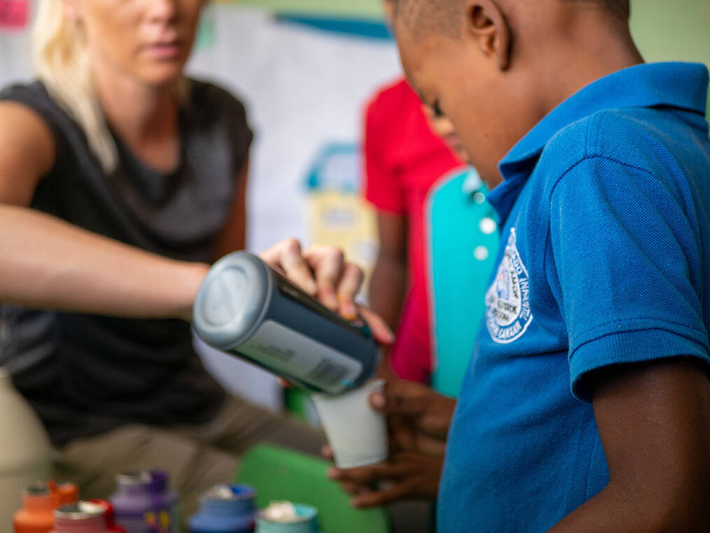 A teacher pouring paint for a students