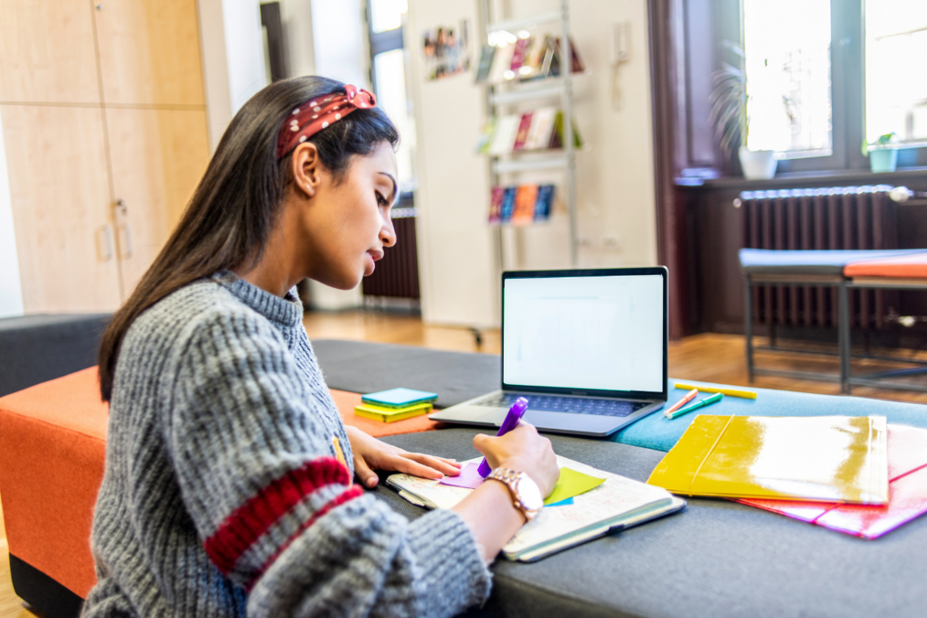 A woman writes on sticky notes with a laptop in front of her.