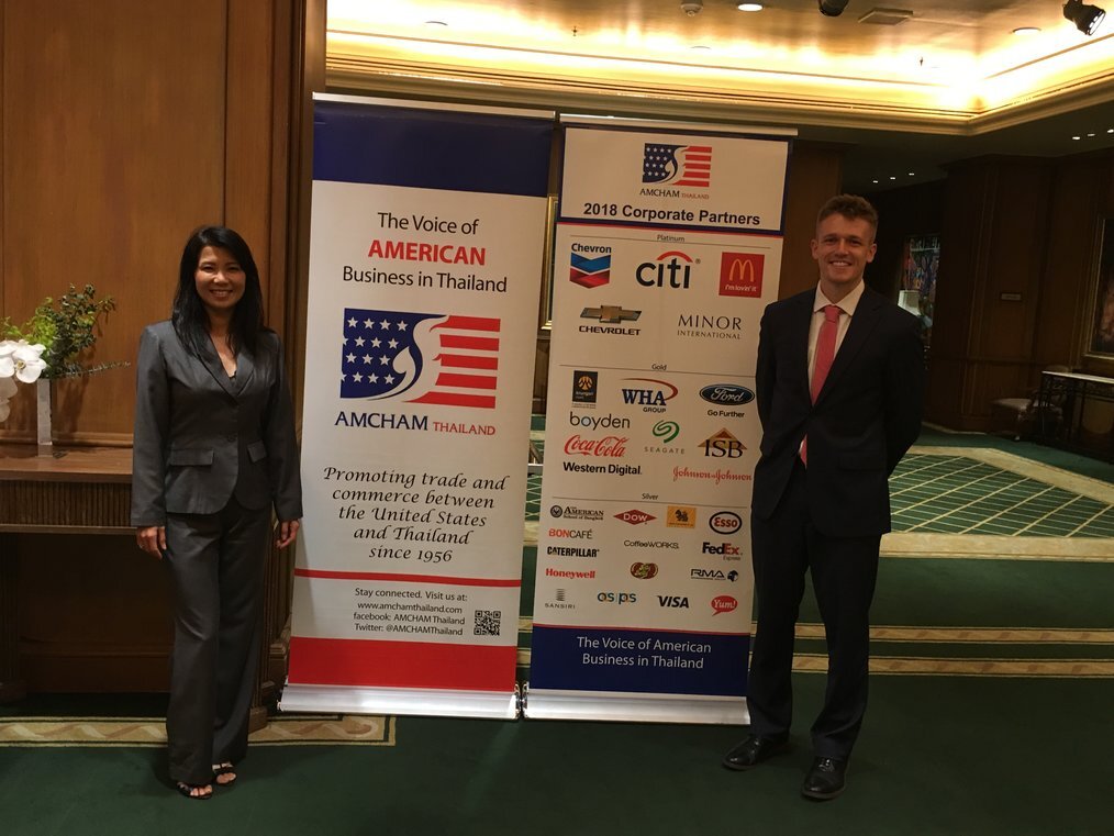 AIP Aa man and a woman in suits stand smiling in front of a poster.