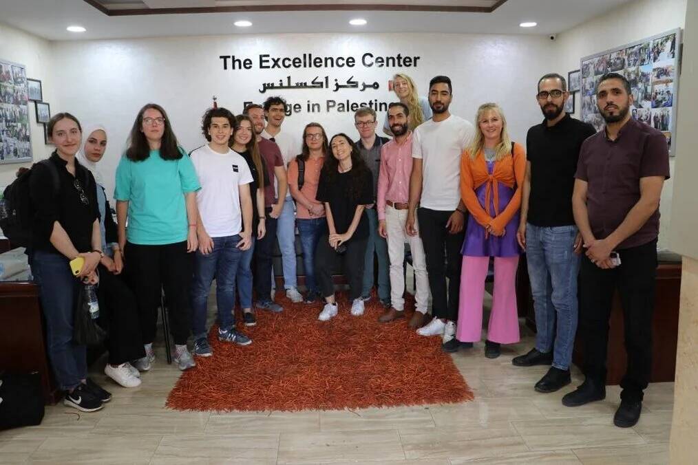 A large group of people smile and pose in front of wall that reads The Excellence Center.