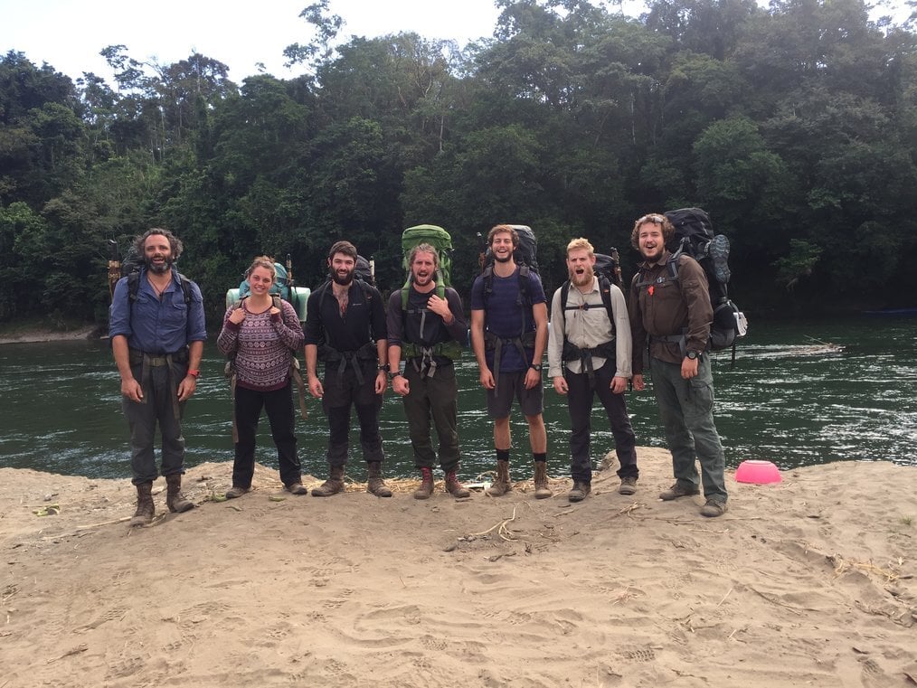 Gapforce A group of people stand on a riverbank with large backpacks.