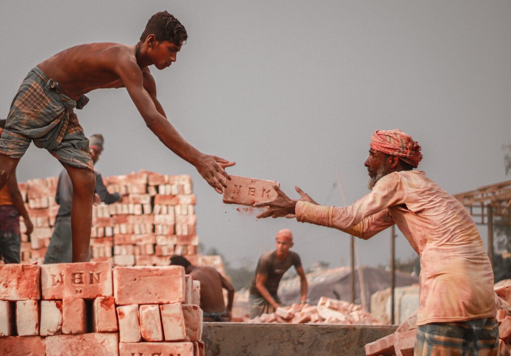 Photo by mohammad samir on Unsplash A man hands another man a large brick.