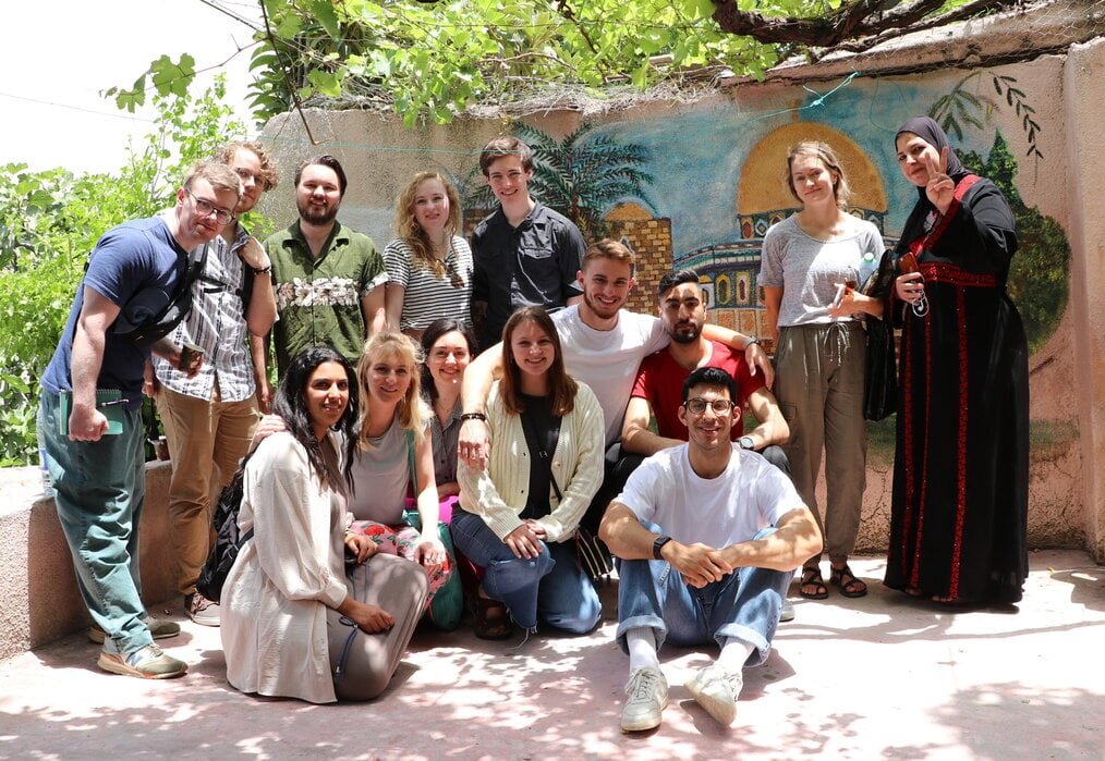 Ex Cent A smiling group of people stand in an outdoor courtyard.