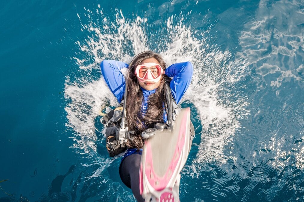 Gili2 A woman plunges backwards into water with scuba gear on.
