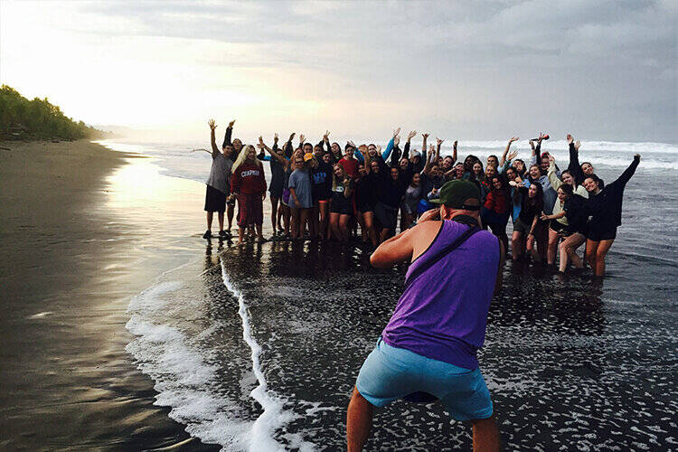 A photographer photographs a group of people standing on the beach.