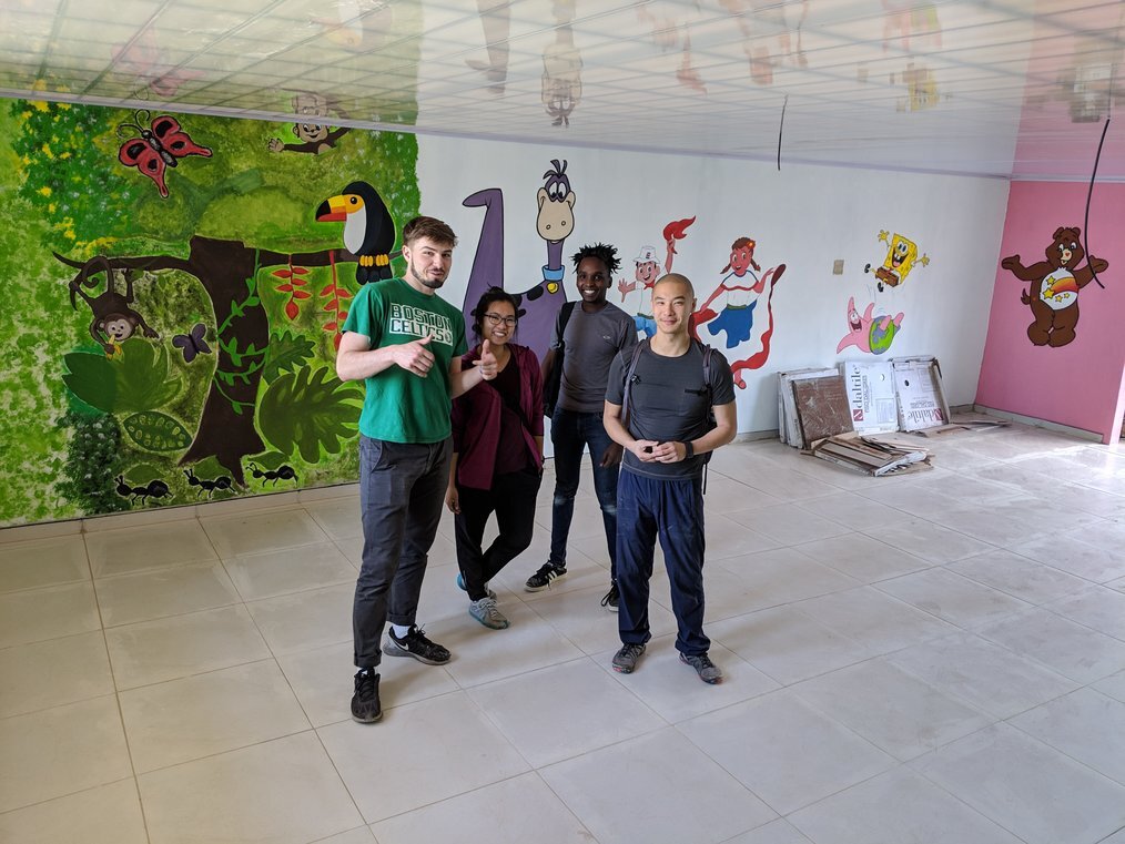 Max Nivel A group of people stand in front of a colorful mural and smile.