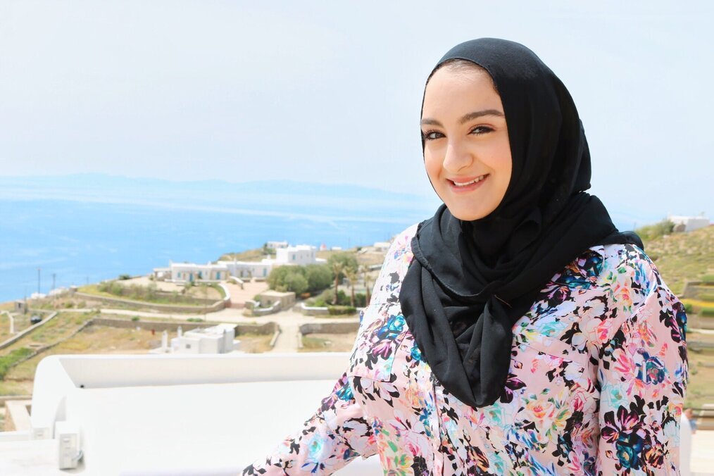 CIS A woman wearing a black hijab smiles with a view of the ocean in the background.