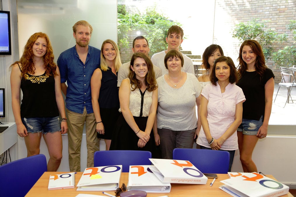 Oxford TEFL A group of people stand around a table with binders on it.