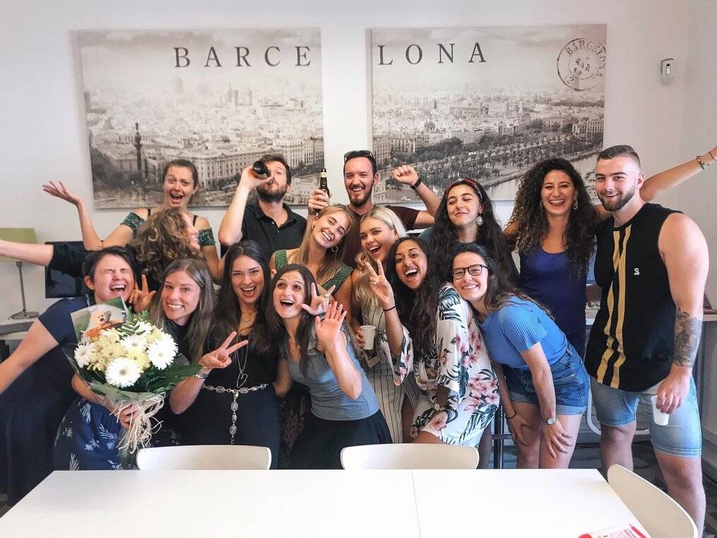 A group of people pose and smile in front of a poster of Barcelona.