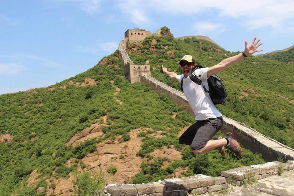 Doug ITA A man jumps in the air smiling on the Great Wall of China.
