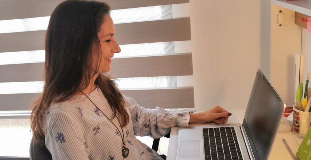 OnTESOL A woman sits smiling and looking at her laptop.