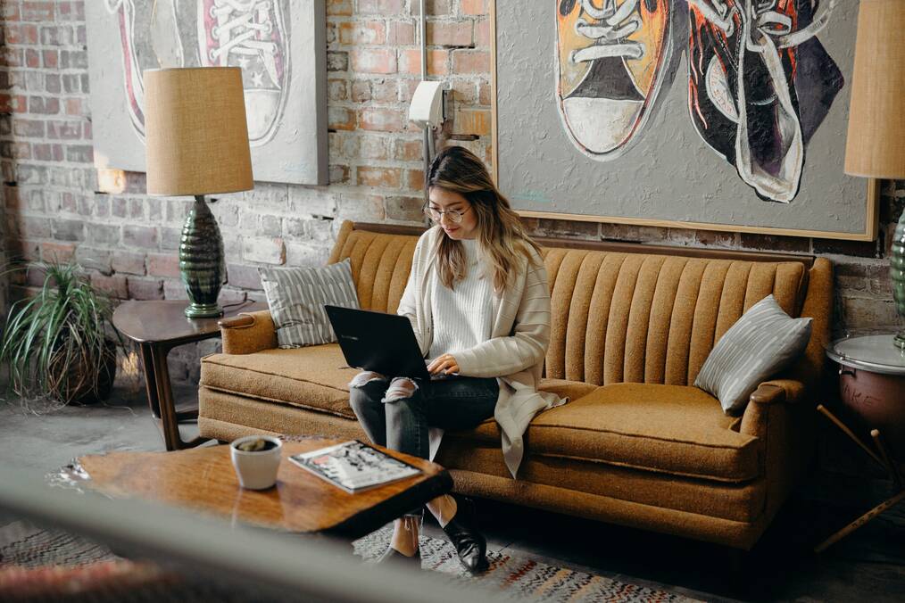 A woman sits on a couch working on a laptop.