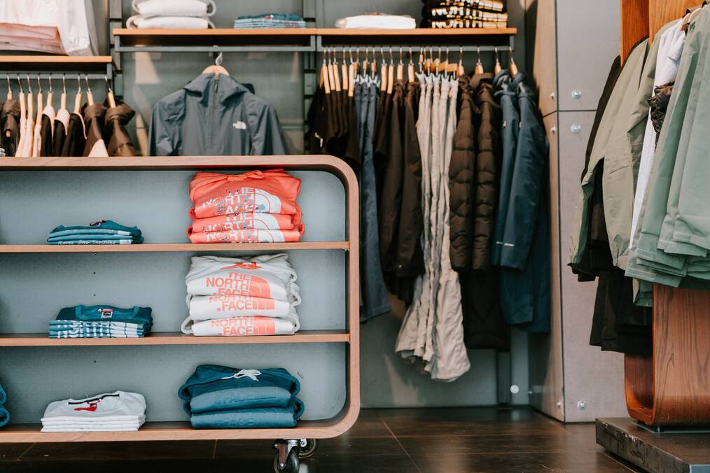 The North Face clothes sit folded on a shelf in a store.
