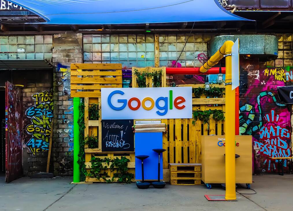 A Google sign hangs on a building with graffiti.