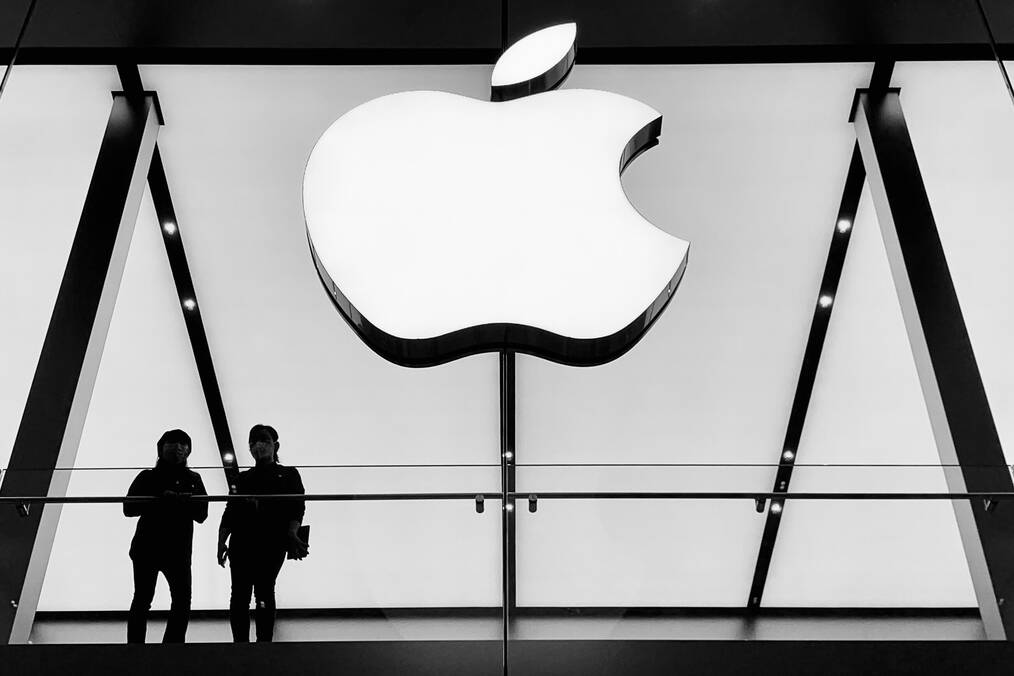 Two people stand under a giant Apple logo.