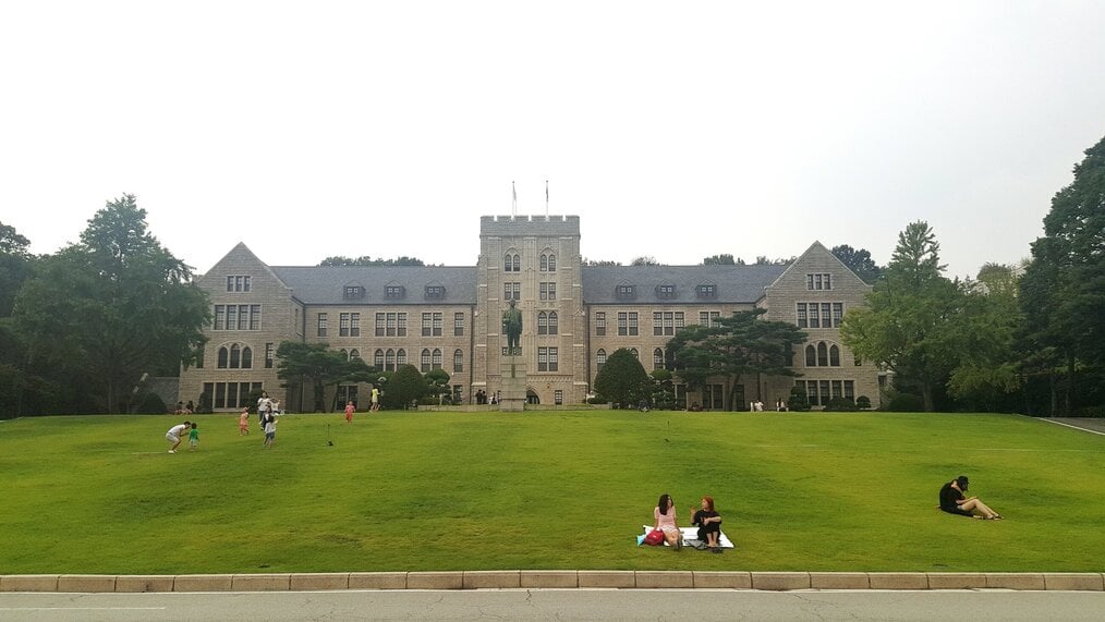 Photo by CYAN via Wikimedia Creative Commons People sit on the lawn in front of a building on the Korea University campus.