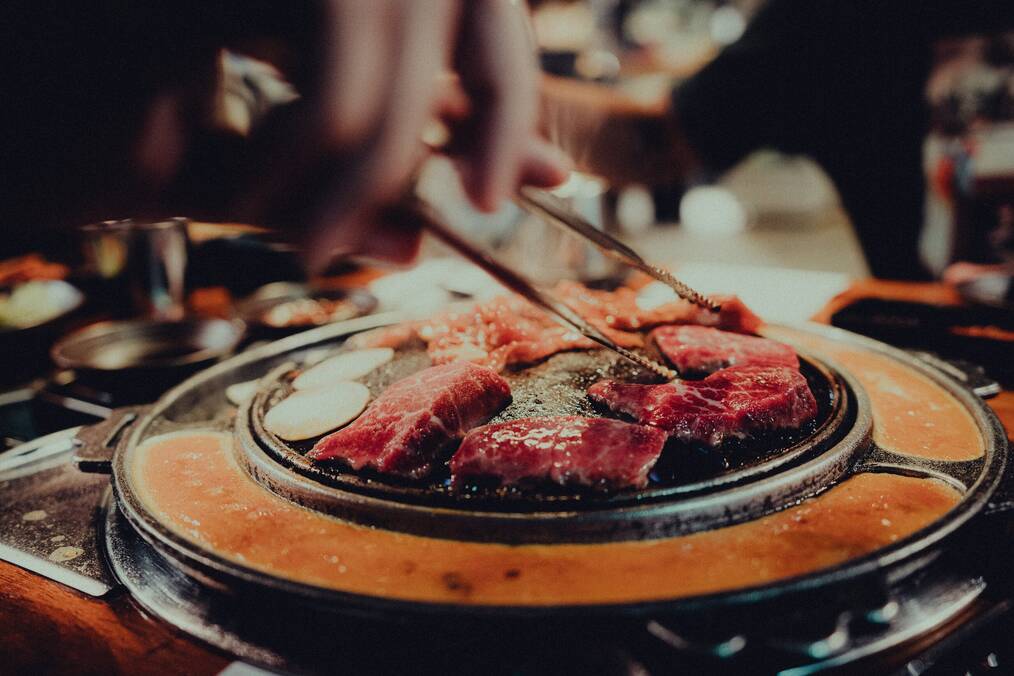 Someone turns meat on a grill with chopsticks.