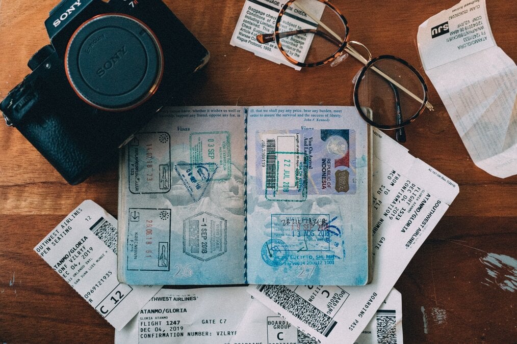 An open passport sits on a table next to a pair of glasses and a camera.