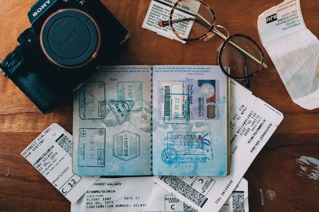 An open passport sits on a table next to a pair of glasses and a camera.